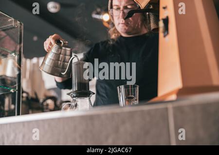 Barista versare acqua calda in aeropress per la preparazione di caffè nero in coffee shop Foto Stock
