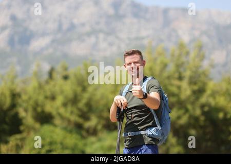 Uomo sorridente con bastoni da passeggio scandinavi e cartello con il pollice in alto Foto Stock