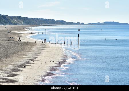 Boscombe, Bournemouth, Dorset, Inghilterra, Regno Unito, 9th luglio 2022, Meteo. Onda di calore a metà estate. La gente arriva alla spiaggia prima delle 8 del sabato mattina. Le temperature raggiungeranno i 20s alti nel pomeriggio sotto il sole parete-parete. Luce brillante e scintillante sul mare. Credit: Paul Biggins/Alamy Live News Foto Stock