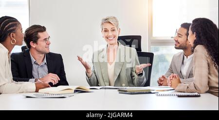 È semplice: Una donna d'affari matura che siede con i suoi colleghi e conduce una riunione in ufficio. Foto Stock