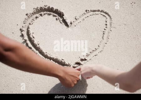 Bene, questo amore è sempre un'inconfondibile coppia che attingerà un cuore nella sabbia della spiaggia. Foto Stock