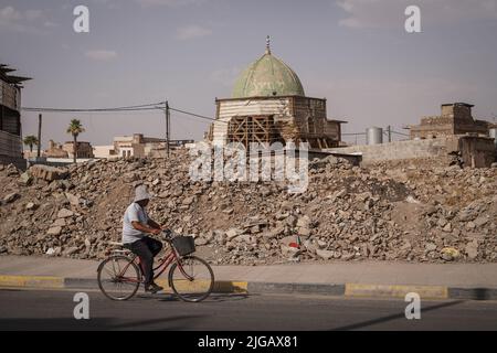 07 luglio 2022, Iraq, Mosul: Un'immagine resa disponibile il 09 luglio 2022 mostra un uomo che cavalcava la sua bicicletta oltre la cupola della Grande Moschea distrutta di al-Nuri nella Città Vecchia di Mosul, cinque anni dalla sua liberazione dal cosiddetto gruppo terroristico dello Stato islamico (IS). Dopo quasi nove mesi di feroci combattimenti, Mosul fu liberato nel luglio 2017 da un'alleanza di forze. Considerata una delle battaglie urbane più dure della storia recente, la battaglia di Mosul ha inflitto pesanti danni a gran parte della città, nonché ai siti storici della città vecchia, per non parlare degli edifici di importanza storica Foto Stock