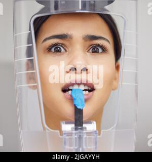 Quanto tempo devo rimanere così: Una giovane donna che guarda ansiosa mentre usa una macchina a raggi X in un ufficio dentistico. Foto Stock