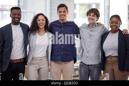 Erano una squadra che vinse costantemente. Un gruppo vario di uomini d'affari che si levano in piedi nell'ufficio con le loro braccia intorno l'un l'altro. Foto Stock