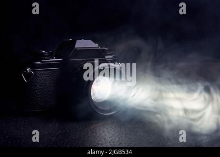 vecchia macchina fotografica con un raggio di luce dall'obiettivo nel fumo su uno sfondo nero Foto Stock