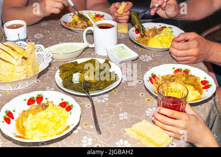 La famiglia mangia al tavolo da pranzo. Dolma su un piatto, salsa e purè di cavolo, tazze con bevande. Foto Stock