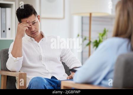 Un bel giovane seduto in clinica con il suo terapeuta e che si sente stressato. Foto Stock