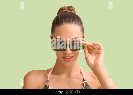 Giovane donna abbronzata in occhiali da sole su sfondo verde, primo piano Foto Stock