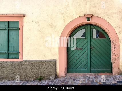 Vecchia porta europea ad arco verde con finestre su una strada di mattoni Foto Stock