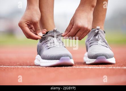 Un atleta femminile irriconoscibile che lega i suoi lacci in pista. Foto Stock