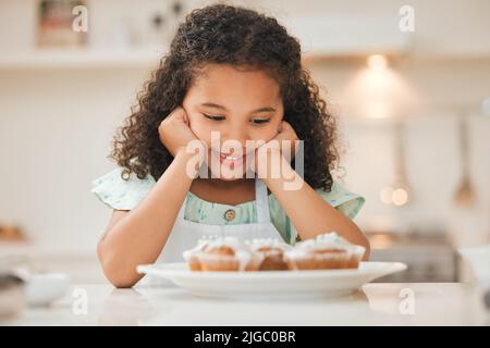 Non so se potessi aspettare più a lungo: Una bambina che aspetta pazientemente di mangiare i cupcake appena sfornati. Foto Stock