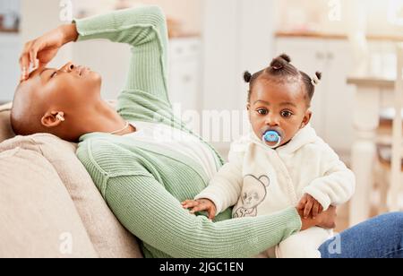 Il bambino viene sempre per primo. Una giovane donna seduta sul divano sua figlia mentre soffre di mal di testa. Foto Stock