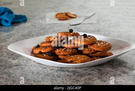 Fuoco selettivo su un mucchio di biscotti di cioccolato in una piastra bianca con la guarnizione di bacche e isolato su uno sfondo di marmo bianco sfocato.Closeup. Foto Stock