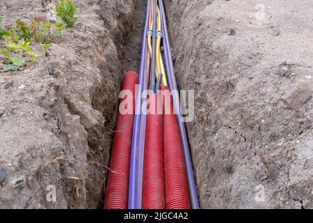 Cavo elettrico sotterraneo. Linee elettriche e a banda larga in vari colori e tipi di tubi. Lavori di collegamento sul cantiere edile. Foto Stock