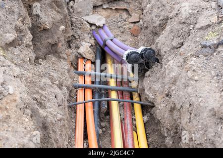 Cavo elettrico sotterraneo. Linee elettriche e a banda larga in vari colori e tipi di tubi. Lavori di collegamento sul cantiere edile. Foto Stock