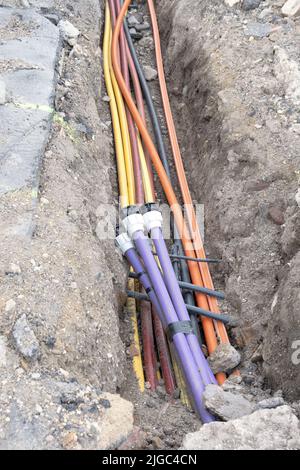 Cavo elettrico sotterraneo. Linee elettriche e a banda larga in vari colori e tipi di tubi. Lavori di collegamento sul cantiere edile. Foto Stock