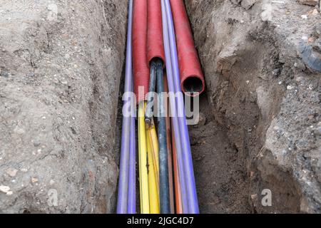 Cavo elettrico sotterraneo. Linee elettriche e a banda larga in vari colori e tipi di tubi. Lavori di collegamento sul cantiere edile. Foto Stock