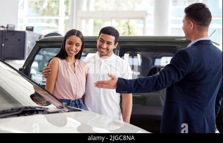 Questa bellezza è appena entrata in. Un venditore di auto che assiste una giovane coppia sul pavimento dello showroom. Foto Stock