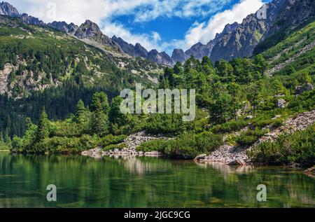 Bellissimo paesaggio estivo di alti Tatra, Slovacchia - lago di Poprad, foresta lussureggiante, rocce in acqua pura, montagne e nuvole bianche sul cielo Foto Stock