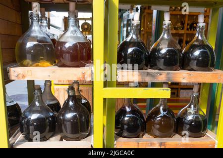 ripiano in legno giallo con varie bottiglie di vetro bulbo caraffe riempite di aceto e vino posto di fronte alla stalla in un mercato Foto Stock