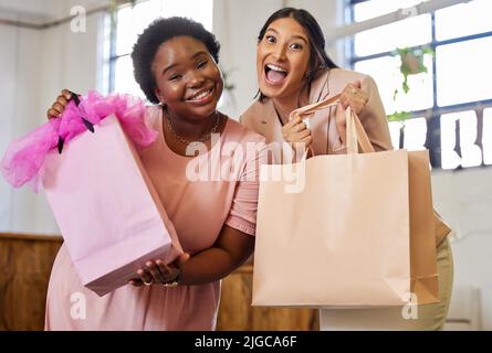 Weve ha ottenuto appena che cosa avete bisogno. Ritratto ritagliato di due attraenti proprietari di affari giovani donne che tengono i sacchetti di shopping mentre si levano in piedi nel loro deposito. Foto Stock