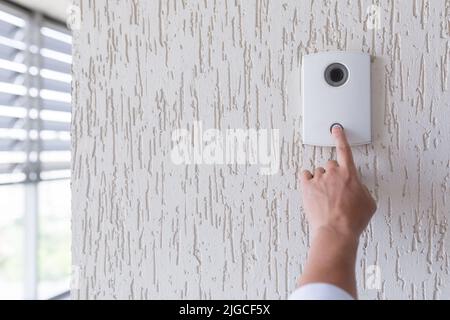 Mano di un uomo in una camicia bianca premendo il pulsante di una porta bussare su una parete bianca di una casa, un intelligente porta bussare con una videocamera per la comunicazione Foto Stock