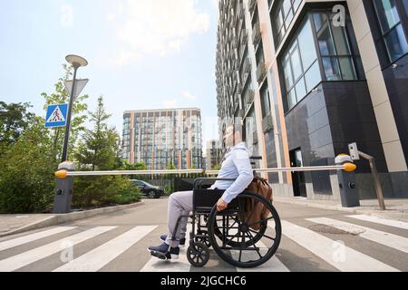Uomo con disabilità pensive seduto su sedia a rotelle all'esterno dell'edificio degli uffici Foto Stock
