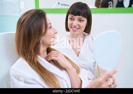 La donna guarda nello specchio dopo iniezioni da rughe sulla fronte Foto Stock