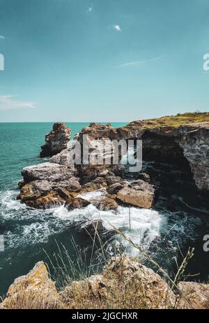 Un colpo verticale di onde che si infrangono su scogliere di mare sotto un cielo blu in una giornata di sole Foto Stock