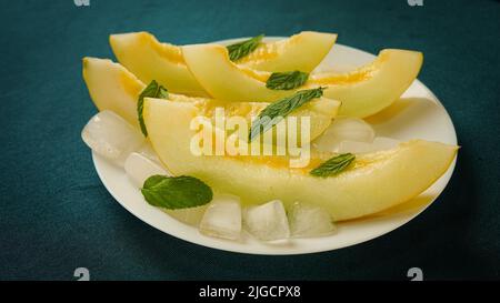 melone maturo con ghiaccio tritato e foglie di menta, tagliato a pezzetti e fette Foto Stock