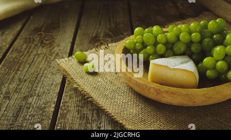 formaggio rustico e uva verde su un tavolo di legno in una fattoria Foto Stock