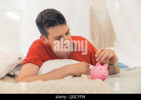 Giovane uomo caucasico che mette denaro nella banca di Piggy. Foto di alta qualità Foto Stock