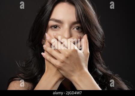 Donna copre la bocca con due mani, non disposto a rivelare qualcosa di importante. Giovane concetto femminile silenzio, paura, violenza. Foto Stock