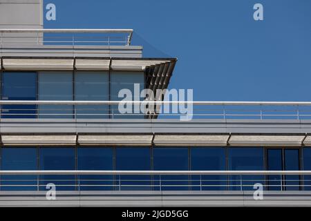 Particolare del tetto e dell'ultimo piano di un edificio moderno con doghe e ringhiere solari orizzontali e cornici verticali delle finestre contro la sica blu brillante Foto Stock