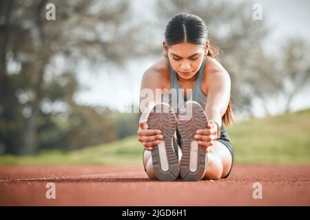 Preparare il corpo per una sfida. Un giovane atleta che allunga le gambe su una pista da corsa all'aperto. Foto Stock