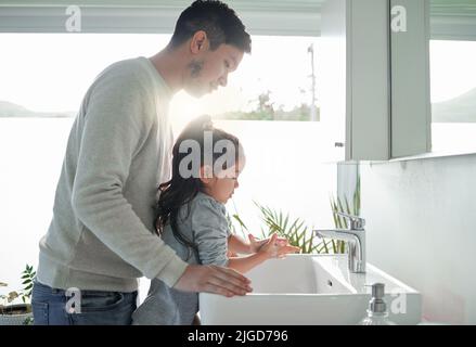 Cominciate i bambini con l'igiene personale, un padre che aiuta sua figlia a lavarsi le mani a un rubinetto in un bagno a casa. Foto Stock