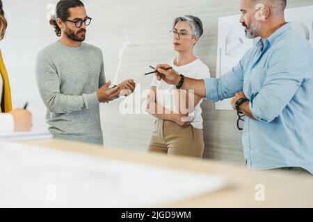 Gruppo di designer creativi che hanno una discussione mentre lavorano con i modelli e i disegni di turbine eoliche 3D. Team di imprenditori innovativi che progettano un r Foto Stock