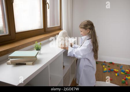 Ragazza piccola allegra nei medici oversize cappotto bianco che gioca ospedale Foto Stock