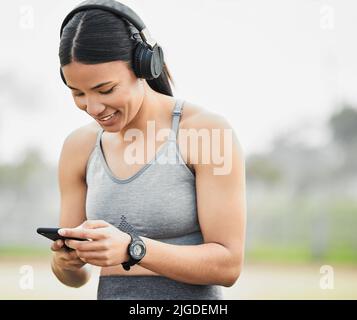 Monitorare i suoi progressi sull'app fitness. Una giovane atleta attraente che controlla i suoi messaggi mentre si esercita all'esterno. Foto Stock