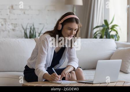 Donna in cuffie si siede sul divano e-learning online utilizzando il laptop Foto Stock