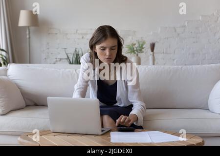 Giovane donna gestire le finanze utilizzando la calcolatrice, pagare le fatture online Foto Stock