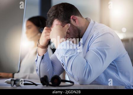 Voglio solo tornare a casa ora: Un giovane agente di call center che guarda stressato mentre lavora in ufficio di notte. Foto Stock