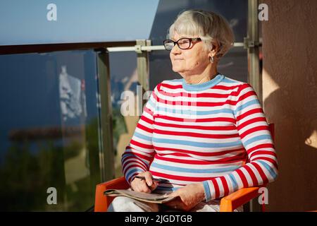 Donna anziana in bicchieri seduti sul balcone vicino al mare Foto Stock