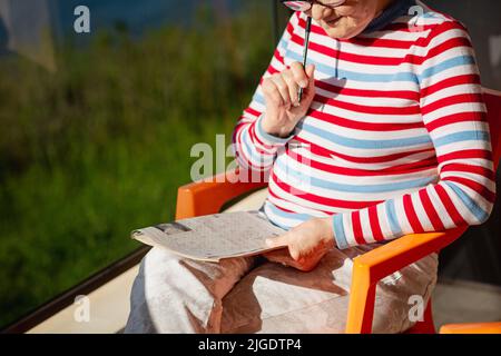 Donna anziana in bicchieri seduti sul balcone vicino al mare Foto Stock