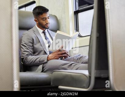 Navigare in metropolitana con un libro a portata di mano. Un giovane uomo d'affari che legge un libro in treno durante il suo tragitto. Foto Stock