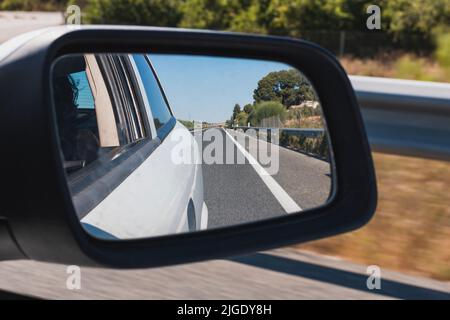 Specchietto retrovisore di una vettura bianca che guida su una strada, riflesso nello specchietto. Sullo sfondo è possibile vedere il movimento di scorrimento dell'este Foto Stock