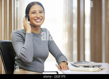 Come posso essere di servizio oggi. Ritratto corto di una giovane e attraente agente di call center femminile che lavora alla sua scrivania in ufficio. Foto Stock
