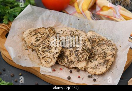Filetto di pollo con erbe aromatiche su pergamena su tavola di legno Foto Stock