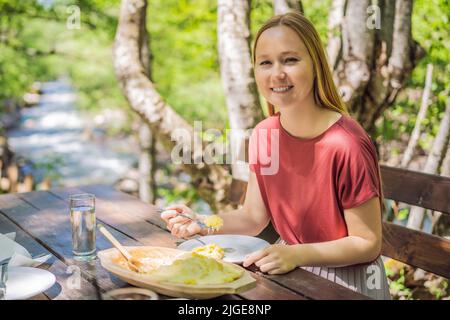 Donna turistica mangiare tradizionale Montenegrin pasto. Kacamak in ciotola di legno nella caffetteria all'aperto Foto Stock