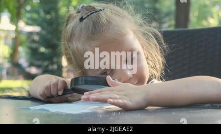 La bambina guarda con attenzione nella lente al sale. Primo piano della ragazza bionda sta studiando i cristalli di sale mentre la guarda attraverso la lente d'ingrandimento Foto Stock